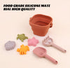 Collapsible sand pail and toys on a sandy surface with text about food-grade silicone.